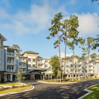 A modern residential apartment complex surrounded by tall trees under a clear blue sky.