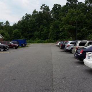 A view of a parking lot bordered by trees, showcasing several parked cars along the side of a winding road.