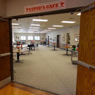 An empty cafe with arranged tables and chairs, viewed from the entrance with a sign overhead.
