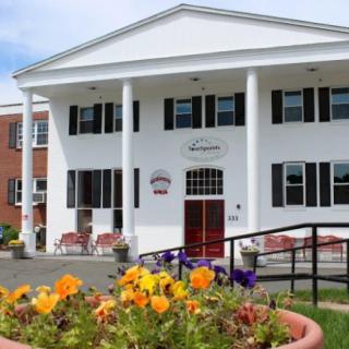 A white building with columns and a vibrant flower bed at the entrance.