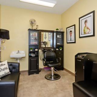 A cozy hair salon interior with a styling station, barber chair, and framed pictures on the walls.