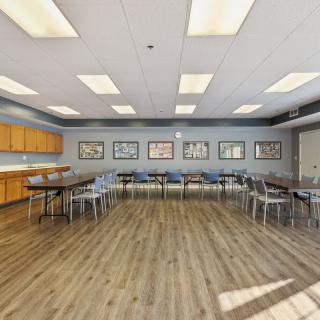 A spacious conference room with tables and chairs arranged for a meeting, featuring artwork on the walls and a wooden floor.