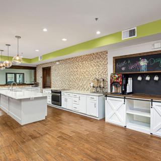 A modern kitchen with white cabinets and a central island, featuring wood flooring and decorative pendant lighting.