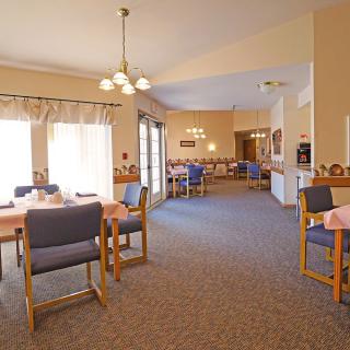 A spacious dining area with multiple tables and chairs, well-lit by ceiling lights and natural light from windows.
