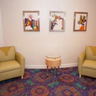 A cozy waiting area with two chairs, a small table, and colorful artwork on the wall.