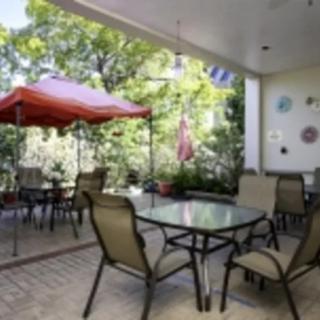 A cozy patio with a table, chairs, and an umbrella, surrounded by lush greenery.