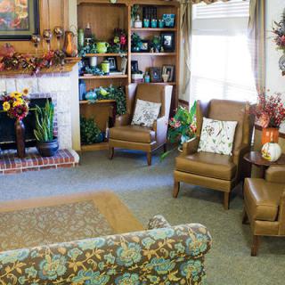 A cozy living room with armchairs, a decorated fireplace, and bookshelves filled with various items.