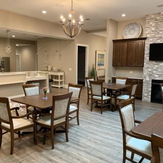 A modern dining area with multiple tables and chairs, featuring a chandelier and a fireplace.