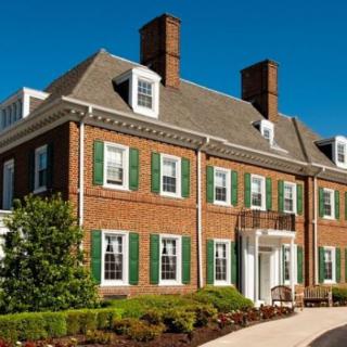 A colonial-style brick house with green shutters and chimneys surrounded by well-maintained landscaping.
