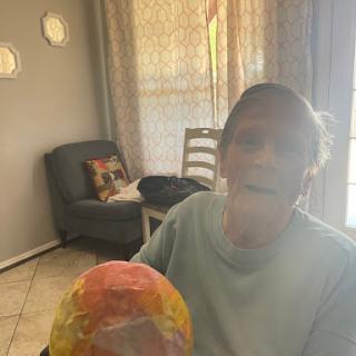 An elderly person joyfully holds a colorful object in a sunlit living room.