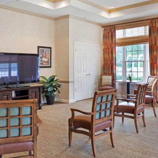 A well-lit living room area with chairs arranged in front of a television and a window with curtains.