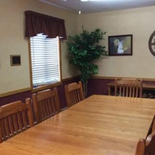 A conference room featuring a large wooden meeting table surrounded by chairs, with a decorative plant and framed pictures on the walls.