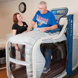 A person undergoing rehabilitation on an anti-gravity treadmill with a therapist providing guidance.