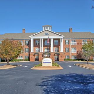 A symmetrical brick building with columns and a landscaped parking area.