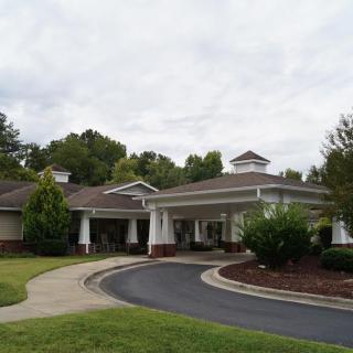 A residential or commercial building with a circular driveway surrounded by greenery and a cloudy sky.