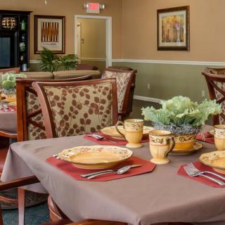 A warmly decorated dining room with set tables, featuring patterned chairs and elegant place settings.