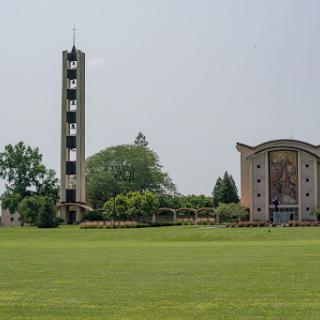 A view of a modern architectural structure featuring a tall tower beside a spacious green field.