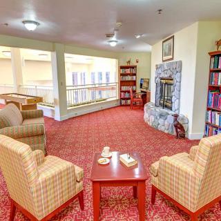 A cozy living room with comfortable chairs, a small table, a fireplace, and bookshelves lining the walls.