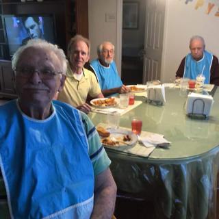 A group of elderly people sitting around a dining table, enjoying a meal indoors.