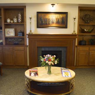 A cozy living room with a central fireplace, bookshelves on either side, and a coffee table adorned with a flower arrangement.