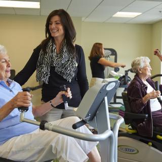 Seniors exercising in a gym with assistance from a trainer.