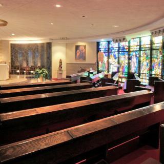 Interior view of a chapel with wooden pews and colorful stained glass windows.