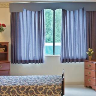 A bedroom with a bed, two dressers, and curtains covering a window.