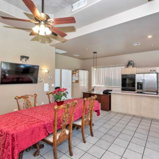 A spacious kitchen and dining area with a ceiling fan, featuring a large dining table draped with a red tablecloth.