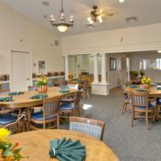 A dining room setup with multiple tables and chairs, decorated with flowers and napkins.