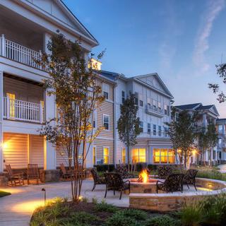 An evening view of a residential apartment complex with outdoor seating around a fire pit.