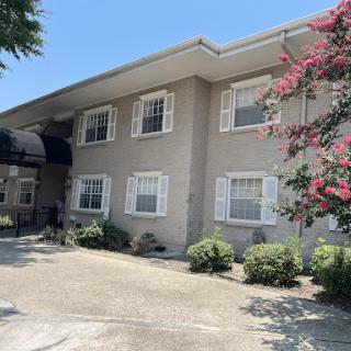 A two-story residential building with a gray exterior and blooming flowers in the foreground on a sunny day.