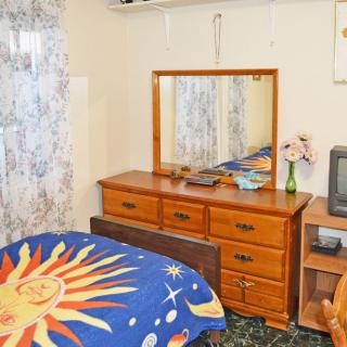 A cozy bedroom with a sun-themed comforter, wooden dresser with a mirror, and a small TV on a stand.