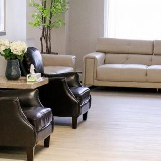 A modern living room with a beige sofa, two black chairs, and decorative plants.