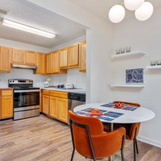 A cozy kitchen with wooden cabinets and a dining area featuring a round table and orange chairs.