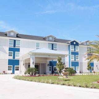 A modern hotel building with a welcoming entrance, surrounded by landscaped greenery and set against a clear blue sky.