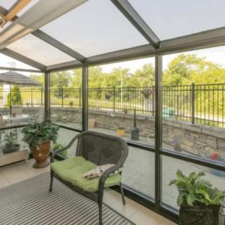 A cozy sunroom with comfortable seating and lush plants, offering a serene view of the outdoors through glass walls.