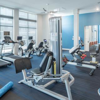 A modern gym with various exercise equipment, including treadmills, stationary bikes, and a weight machine.