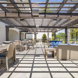 A modern outdoor patio with tables and chairs under a pergola, bathed in sunlight.