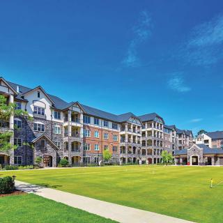 A modern residential apartment complex with a large green lawn under a clear blue sky.