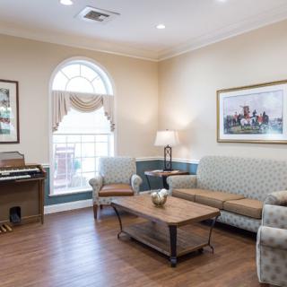 A cozy living room with a sofa, armchair, coffee table, and an organ near a large window.