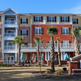 A multi-story apartment building with balconies and palm trees in front.