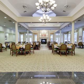 An elegant and spacious dining room with multiple tables, chandeliers, and a carpeted floor.