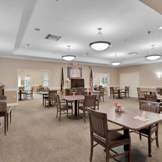 Spacious dining area with multiple tables and chairs, featuring overhead lighting and flags.