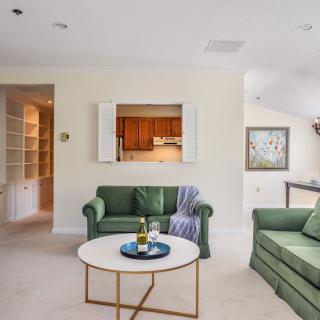 A cozy living room with green couches and a round coffee table, featuring a kitchen pass-through.