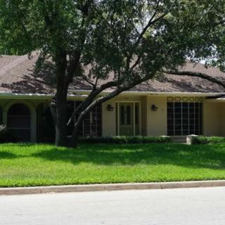 A suburban house with a large tree and well-maintained lawn.