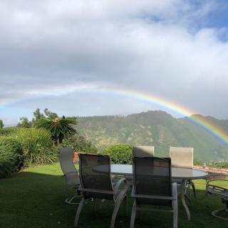 A beautiful rainbow arcs over a scenic garden setting with a table and chairs.