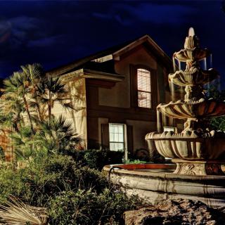 A beautifully lit house at night with a prominent fountain in the foreground.