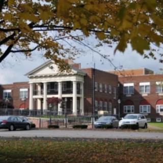 A classic brick building with white columns surrounded by autumn foliage and parked cars.