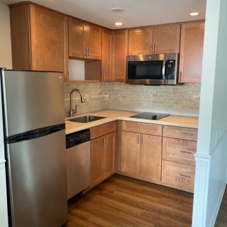 A modern apartment kitchen with wooden cabinets and stainless steel appliances.