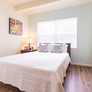 A bright and cozy bedroom with a neatly made bed, bedside table, and artwork on the wall.